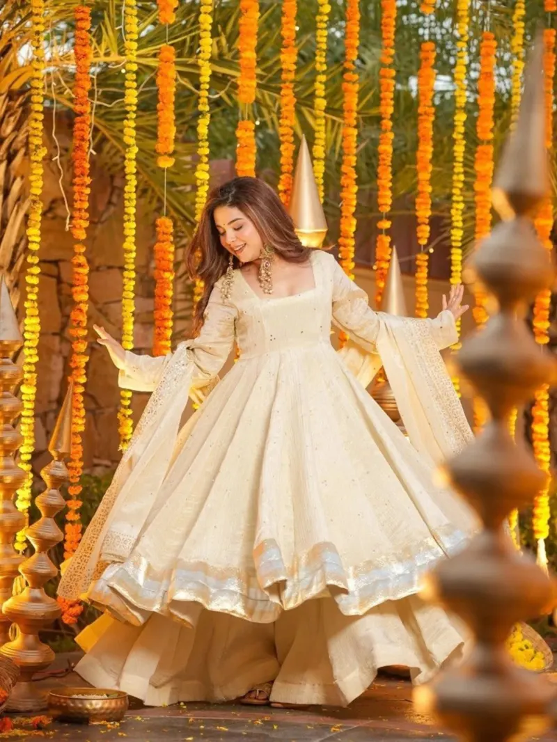 A model twirling in an ivory anarkali with a gold-trimmed hem and dupatta, framed by marigold garlands